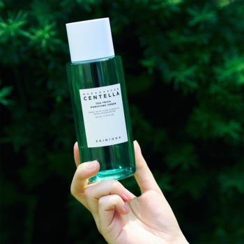 Łagodzący toner do twarzy Skin1004 Centella w zielonej butelce, trzymany w dłoni na tle zielonych liści.
