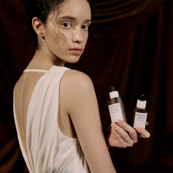 Dwie brązowe butelki serum Centella Probio-CICA Ampoule, trzymane przez modelkę w białej sukni. Skóra wrażliwa.