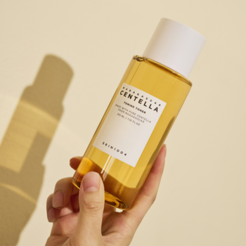 Skin 1004 Madagascar Centella Toning Toner, bursztynowy tonik złuszczający w przezroczystej butelce trzymanej w dłoni.