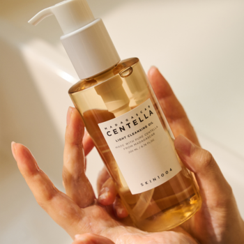 Przezroczysta butelka Skin1004 Madagascar Centella Light Cleansing Oil z białym dozownikiem, trzymana w dłoniach.