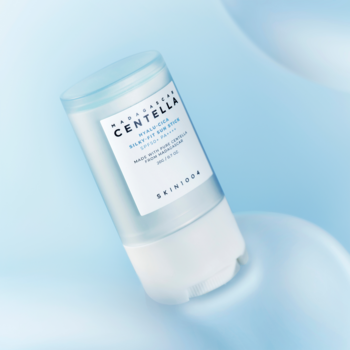 Biało-niebieski sztyft SKIN1004 Madagascar Centella SPF50+, nawilżający, ułożony pod kątem na rozmytym tle błękitnych form.
