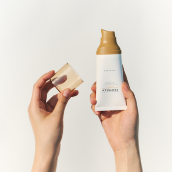 Krem Skin1004 Madagascar Centella Air-Fit Suncream Light, biała tubka z brązowym dozownikiem w dłoniach, odkręcona nakrętka.