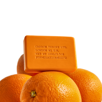 Carbon Theory Vitamin C & Caffeine Facial Cleansing Bar, pomarańczowa kostka myjąca na tle dojrzałych pomarańczy.