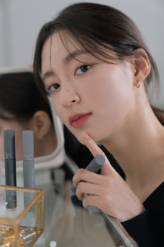 Kobieta z rom&nd Han All Fix Mascara w szarej tubce. Czarny, wodoodporny tusz pogrubiający rzęsy, widok z przodu.