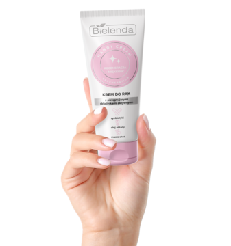 Biało-różowa tubka kremu do rąk Bielenda Handy Cream, trzymana w dłoni z różowymi paznokciami.