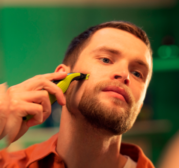 Mężczyzna stylizuje zarost zieloną maszynką Philips OneBlade QP2724-23 przed lustrem.