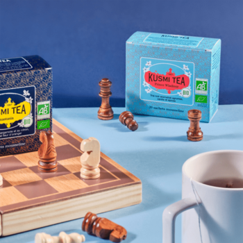Kusmi Tea: dwa pudełka czarnej herbaty cytrusowo-waniliowej na szachownicy z figurami i kubkiem.