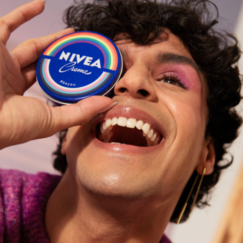Uśmiechnięta osoba z makijażem trzyma krem NIVEA #BeYou z tęczą do oka, nawilżacz do twarzy i ciała.