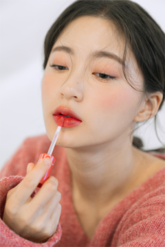 Kobieta nakłada na usta Rom&nd Juicy Lasting Tint w odcieniu Koral Litchi, ukazując jego błyszczący efekt.