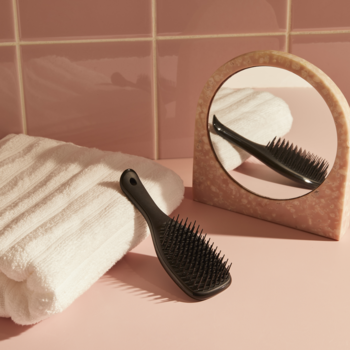 Czarna szczotka Tangle Teezer z rączką na różowym blacie łazienki, do delikatnego rozczesywania mokrych i suchych włosów.