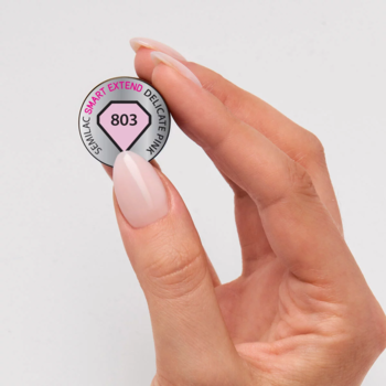 Zbliżenie dłoni z różowymi paznokciami trzymającej metalowy wzornik lakieru Semilac Smart Extend 803 Delicate Pink.