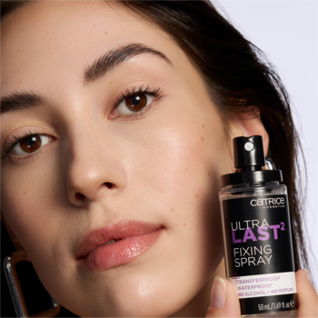 Modelka prezentuje wodoodporny utrwalający spray Catrice Ultra Last2 w czarnej butelce z fioletową etykietą.