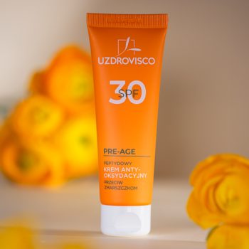 Pomarańczowa tubka UZDROVISCO SPF 30 Pre-Age, peptydowy krem przeciw zmarszczkom, widok z przodu na rozmyte tło.