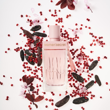Różowa butelka Women'Secret Intimate EDP, otoczona różowym pieprzem i fasolką tonka na białym tle.