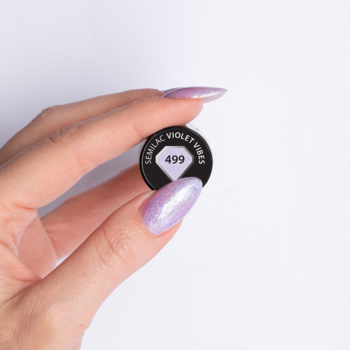 Zbliżenie dłoni z brokatowymi fioletowymi paznokciami i czarnym słoiczkiem lakieru Semilac 499 Violet Vibes.