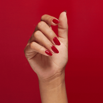 OPI Nail Envy Big Apple Red: Zbliżenie dłoni z długimi, czerwonymi paznokciami na soczystym czerwonym tle.