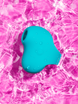 Teal Lovehoney Mon Ami Finger suction stimulator with water droplets, floating on rippled pink water, top-down view.