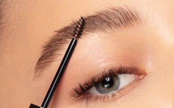 Zbliżenie na oko, brązowe brwi rozczesywane czarną szczoteczką Pupa Plump&Care Eyebrow Gel.