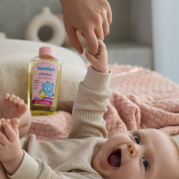 Hipoalergiczna oliwka Bambino dla dzieci, żółta butelka z niebieskim misiem, obok niemowlaka chwytającego dłoń.