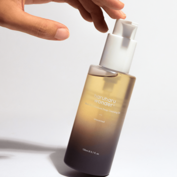 Dłoń trzyma ukośnie olejek do demakijażu Haruharu Wonder Black Rice w butelce ombre z białą pompką.