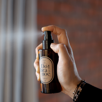 Ręka rozpyla mgiełkę zapachową 'Dobranoc!' 150ml z olejkami eterycznymi z bursztynowej butelki.
