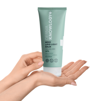 Lekki balsam lipidowy DermaKnowlogy MD02 92% do suchej skóry w zielonkawej tubie, trzymany w dłoniach.