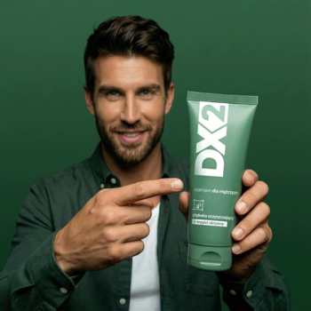 Mężczyzna uśmiecha się i wskazuje na zieloną tubę szamponu DX2 z aktywnym węglem dla mężczyzn.