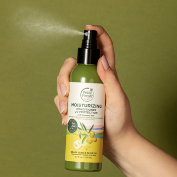 Ręka spryskuje zieloną odżywką Petal Fresh UV Protection z winogron i oliwek, z widoczną mgiełką.