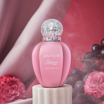 Lou De Pre Kashmir Pink, różowa woda perfumowana w rzeźbionej butelce z brokatową zakrętką, na postumencie.