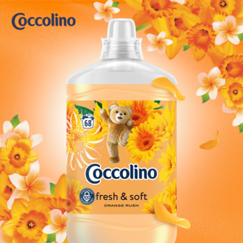 Pomarańczowa butelka płynu do płukania Coccolino Fresh & Soft Orange Rush 68 prań, z misiem, na tle kwiatów.