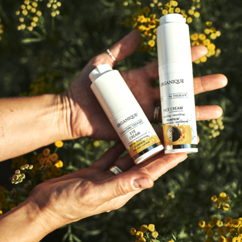 Biały krem pod oczy Skin Revolution z dynią i kofeiną, obok kremu do twarzy, trzymane w dłoniach na tle roślin.