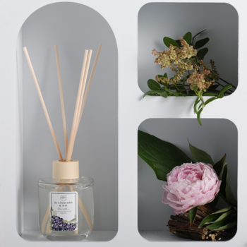 Dyfuzor zapachowy Aroma Home Blackberry&Bay 100ml z patyczkami w szklanej butelce, w jasnej, łukowej niszy, obok kwiatów.