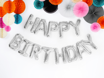 Srebrny balon foliowy "Happy Birthday" z metalicznym wykończeniem i kolorowymi papierowymi kulami na białym tle, z góry.