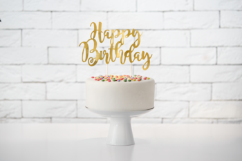 Złoty lustrzany topper na tort 'Happy Birthday', 22.5 cm, na białym torcie z posypką, widok z przodu.