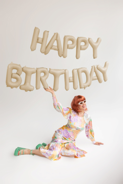 Beżowy, metalizowany balon foliowy „Happy Birthday”, dekoracja urodzinowa, trzymany przez kobietę.