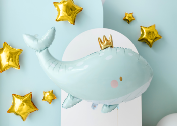 Balon foliowy PartyDeco: jasnoniebieski wieloryb w złotej koronie, otoczony złotymi gwiazdkami, na jasnoniebieskim tle.