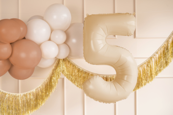 Beżowy balon foliowy cyfra 5, element dekoracji z girlandą z białych i brązowych balonów na ścianie.
