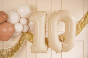 Zbliżenie na beżowe balony foliowe w kształcie liczby 10, otoczone girlandą i mniejszymi balonami.