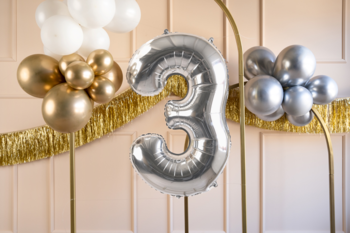 Srebrny balon foliowy cyfra 3 z metalicznym połyskiem, idealny na urodziny, na tle złotych dekoracji.