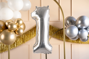 Srebrny balon foliowy cyfra 1 z metalicznym połyskiem, widoczny z przodu na tle złotych dekoracji.
