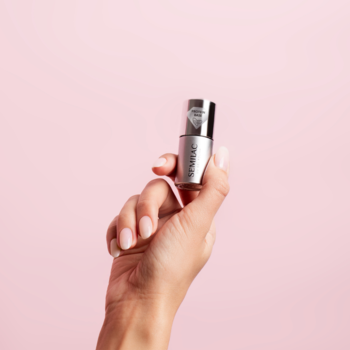 Dłoń trzyma srebrną buteleczkę Semilac Extend Protein Base z jasną nakrętką na różowym tle.