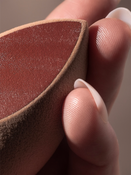 Real Techniques Makeupsaver Sponge. Zbliżenie na beżową gąbkę z czerwonawą teksturą technologii odcisków palców, w dłoni.