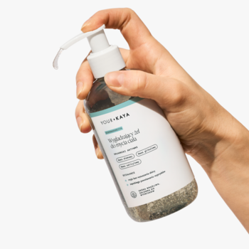 Ręka trzyma wygładzający żel do mycia ciała YOUR-KAYA w butelce z pompką, na białym tle.