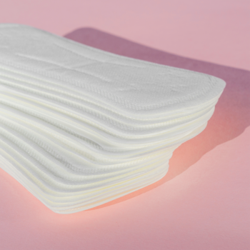 Białe organiczne wkładki higieniczne Joni, stos cienkich bawełnianych wkładek na pastelowym różowym tle.