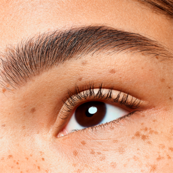 Zbliżenie na brązowe oko z gęstym, podkreślonym brwiom i piegami, efekt pudru Essence Brow Powder Duo.