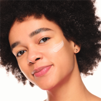 Młoda kobieta z kreską Essence Silky Blur Poreless Primer na policzku, przygotowująca skórę do makijażu.