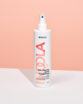 Indola Hair Therapy Spray Conditioner, biała butelka ze sprayem, pomarańczowy napis, widok z przodu na pastelowym tle.