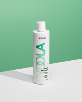 Biała butelka wegańskiego szamponu Indola Repair Shampoo z zielonym logo, widok z przodu na zielono-białym tle.