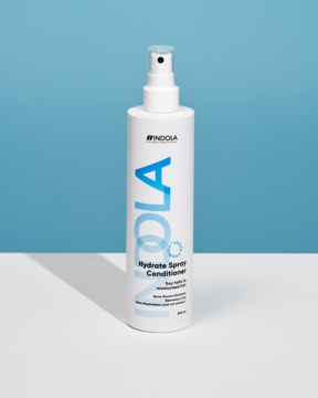 Biała butelka odżywki Indola Hydrate Spray Conditioner z niebieskimi literami "INDOLA", widok z przodu.