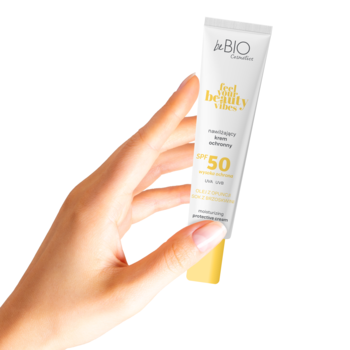 Dłoń trzyma nawilżający krem do twarzy beBIO Feel Your Beauty Vibes SPF 50+ w biało-żółtej tubce.